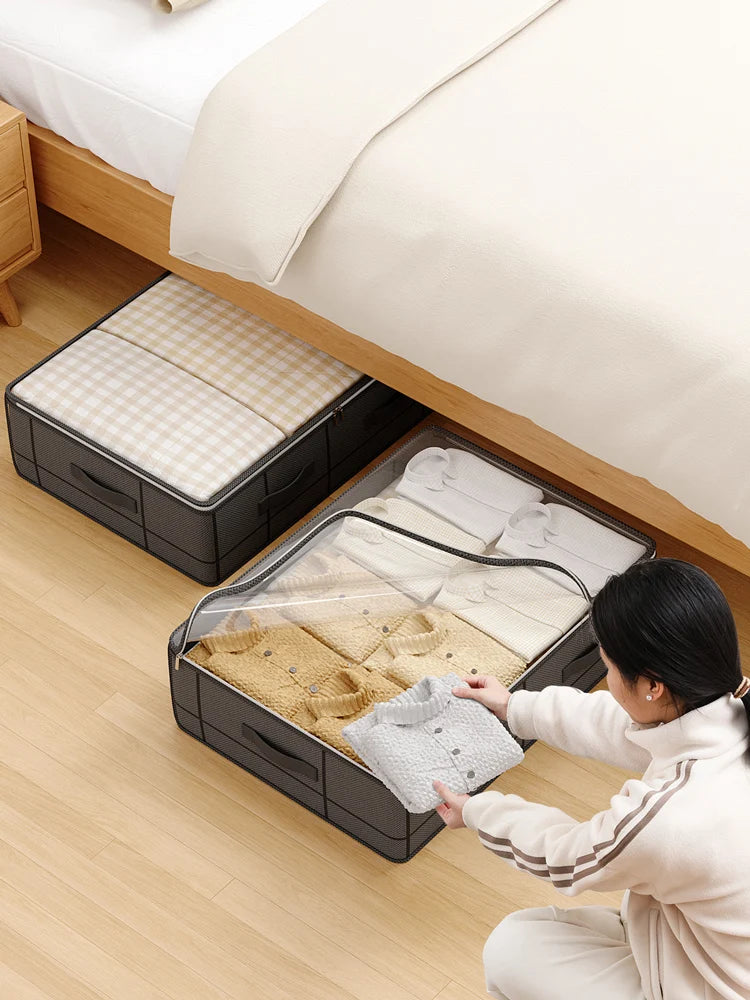 A woman is placing folded baby clothes into a foldable under-bed storage box with a clear window.