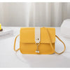 A yellow fashion square crossbody bag with a white strap and gold-colored charm resting on a white surface.