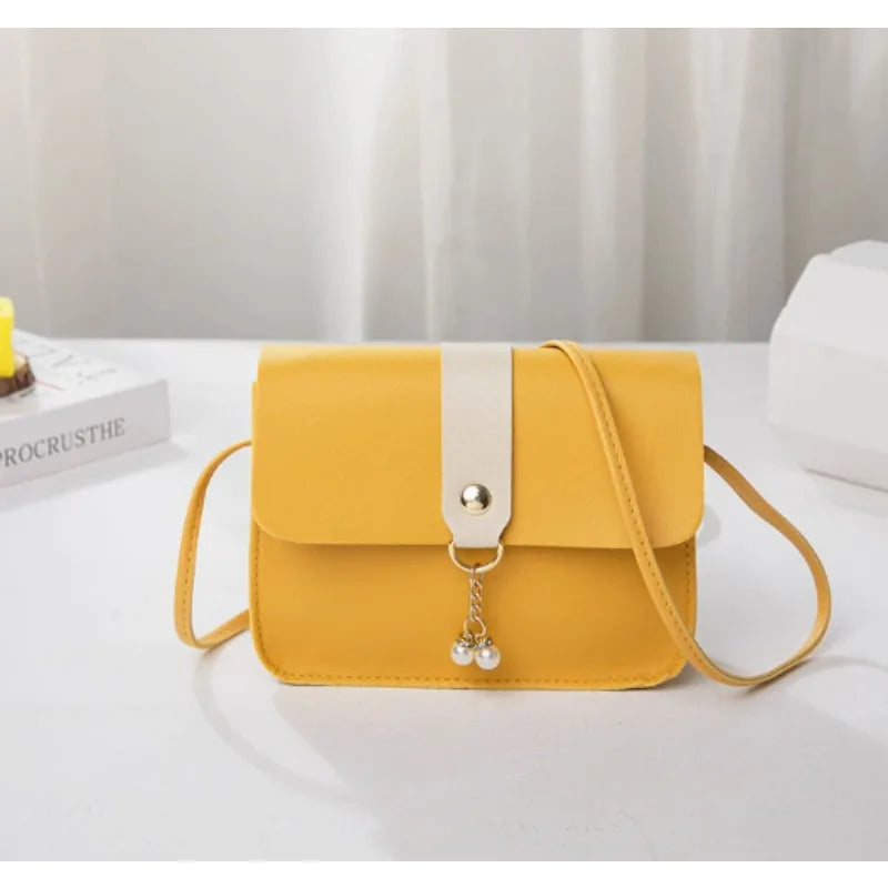 A yellow fashion square crossbody bag with a white strap and gold-colored charm resting on a white surface.