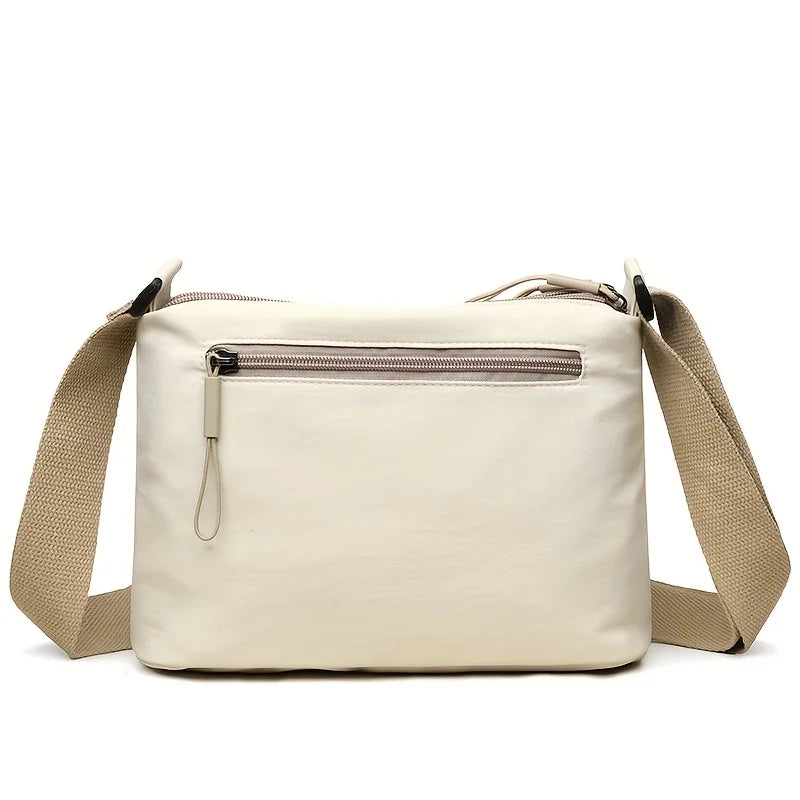 A cream-colored nylon crossbody shoulder bag with a zippered top compartment and tan strap.