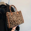 A close-up of a leopard print faux fur designer shoulder tote bag with brown leather handles being held by a person.
