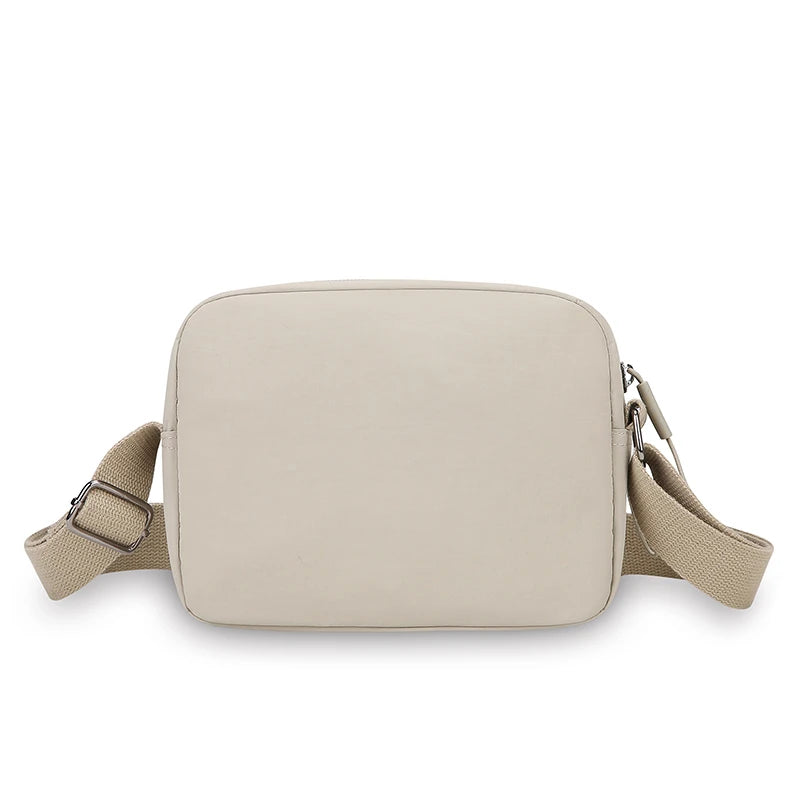 A beige nylon crossbody bag with an adjustable wide strap shown from the front.