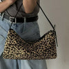 A close-up of a leopard print vintage horsehair and cowhide crossbody bag worn by a person with light gray clothing.