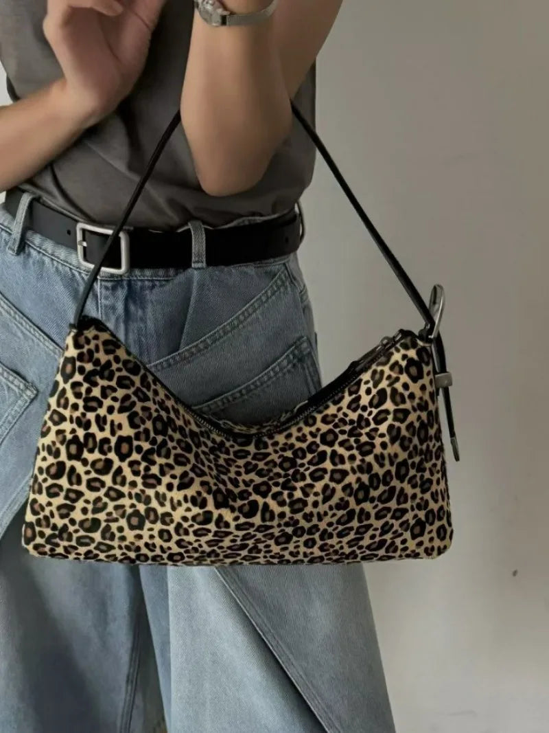 A close-up of a leopard print vintage horsehair and cowhide crossbody bag worn by a person with light gray clothing.