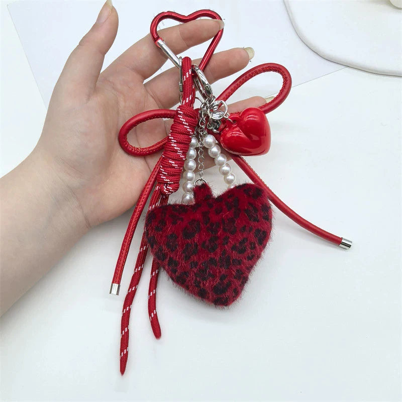 A red and black leopard print faux fur charm keychain with silver hardware is held in a hand.