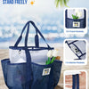 A navy blue mesh beach tote bag with shoulder straps and front and interior pockets resting on sand.
