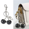 Silver crystal fruit charm keychain with a leaf design attached to a light-colored bag.
