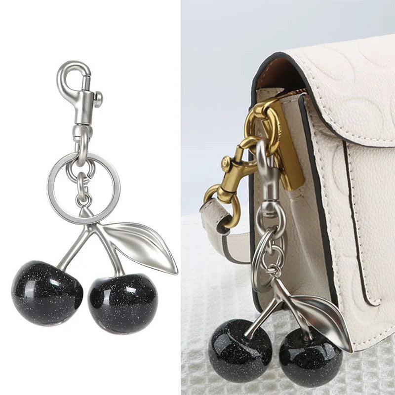 Silver crystal fruit charm keychain with a leaf design attached to a light-colored bag.