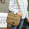 A person is holding a tan canvas tool bag with multiple pockets against a gray background.