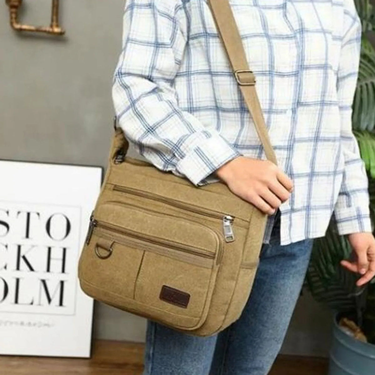 A person is holding a tan canvas tool bag with multiple pockets against a gray background.