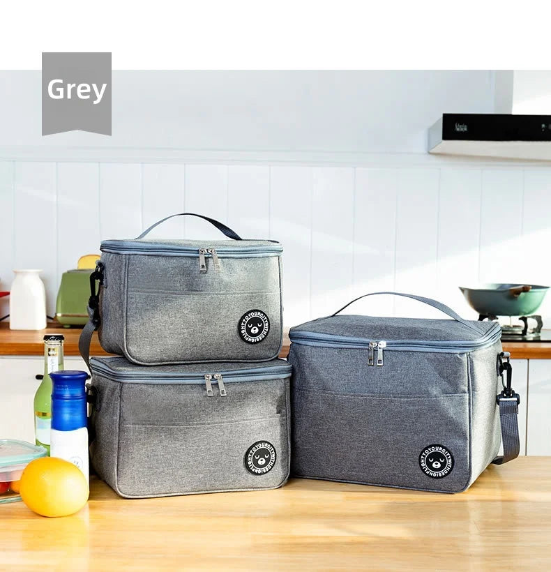 Zwei graue isolierte Thermotaschen liegen auf einem Holztisch in einer hellen Küche.