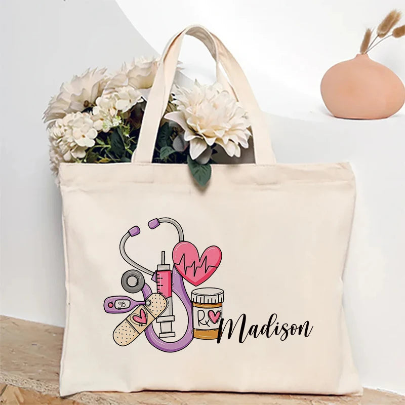 A beige canvas tote bag featuring a graphic design of a stethoscope, heart, and pills with the name Madison.