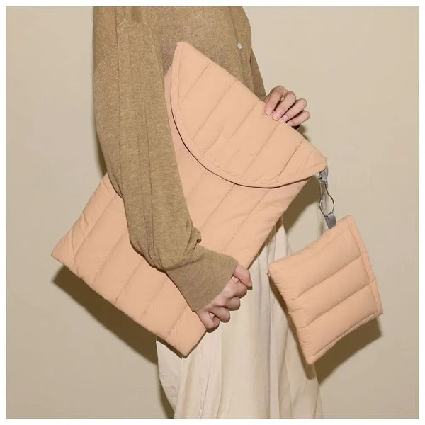 A person is holding a light peach embroidered cotton laptop sleeve over a beige shirt.