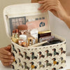 A beige quilted cosmetic travel bag with a dachshund print is shown open, revealing makeup and skincare products.
