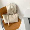 Sac à main beige en cuir PU, posé sur une surface en bois à côté d'un ordinateur portable argenté.