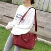A woman is holding a maroon nylon tote bag with a shoulder strap outdoors.