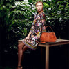 A woman models an elegant leather crossbody shoulder bag in a floral print dress outdoors.