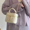 Un petit sac bandoulière beige clair en duvet avec une chaîne dorée, tenu par une personne portant un blazer mauve.