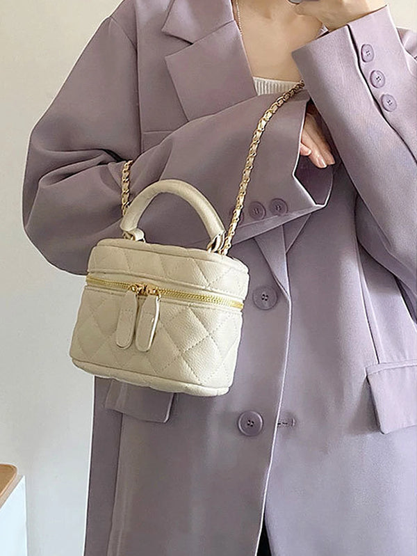 Petit sac bandoulière beige, matelassé, avec une chaîne dorée, tenu par une personne portant un blazer mauve.