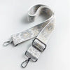 A beige and white jacquard strap for a crossbody bag, featuring a textured pattern and silver hardware.