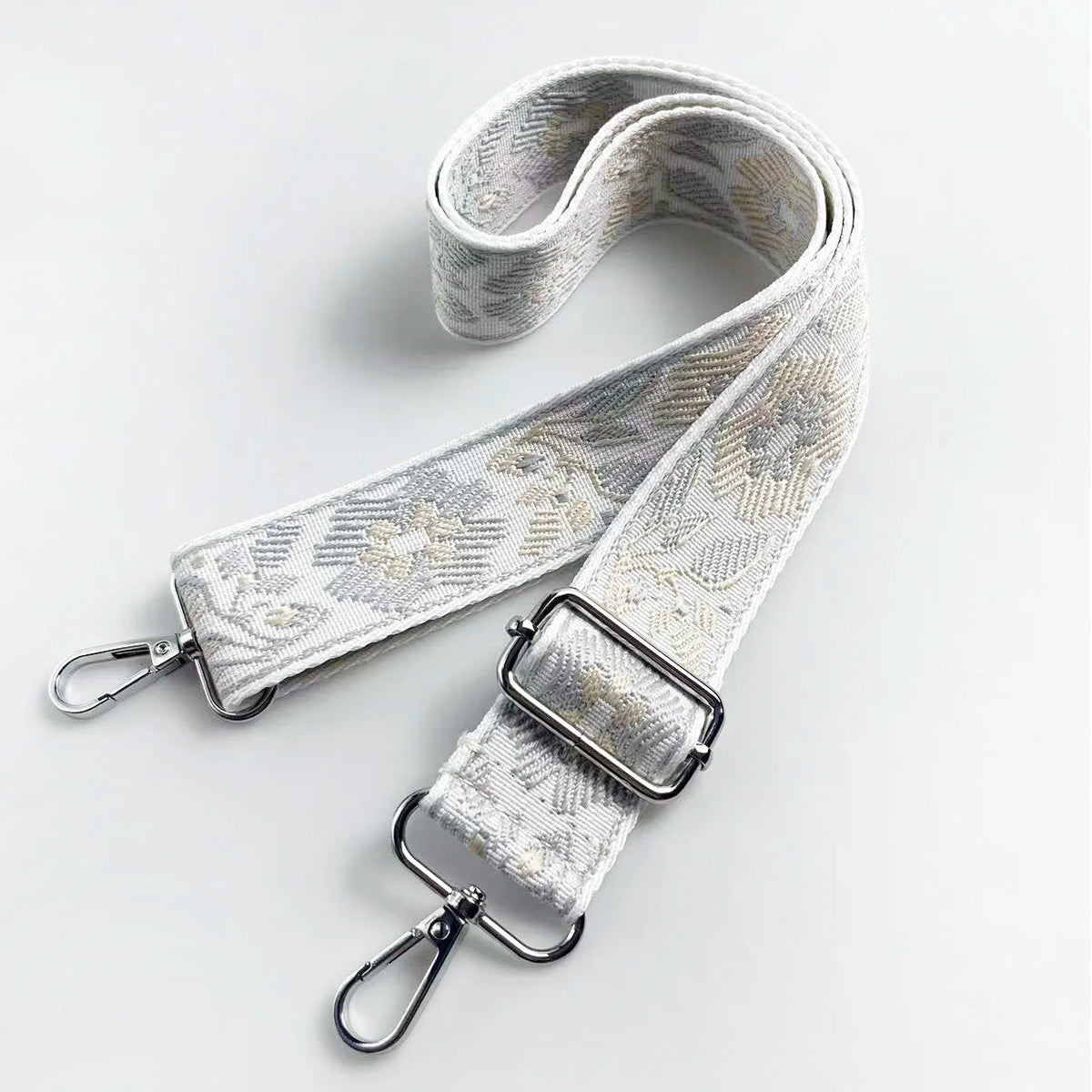 A beige and white jacquard strap for a crossbody bag, featuring a textured pattern and silver hardware.