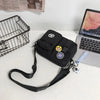 A black quick-dry canvas shoulder bag with a strap and charm resting on a white surface next to a laptop.