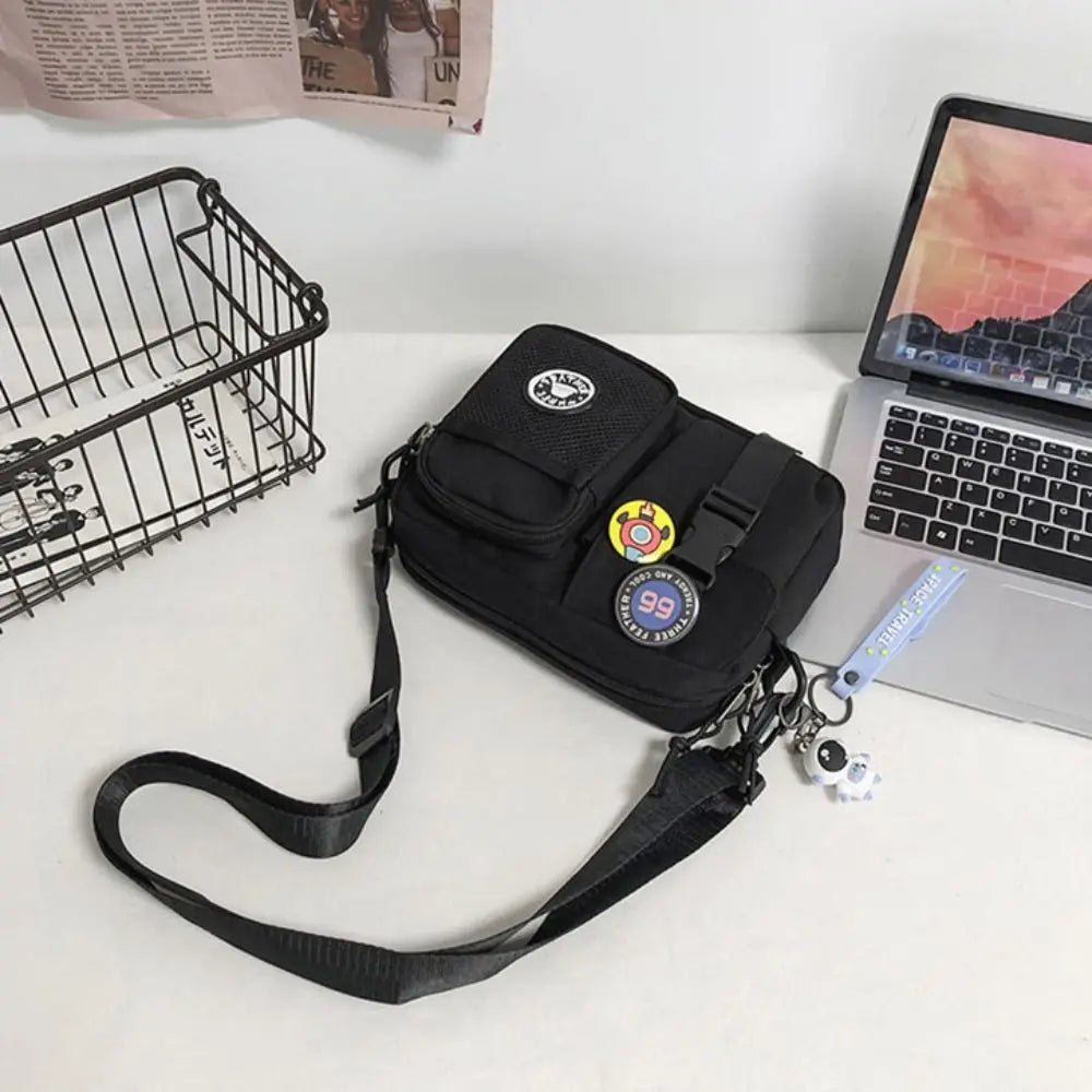 A black quick-dry canvas shoulder bag with a strap and charm resting on a white surface next to a laptop.
