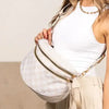 Eine Frau hält eine weiße karierte Crossbody-Tasche und beige Hosen.