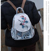 A woman wearing a dark coat carries a light gray linen backpack with pink and blue 3D embroidery.