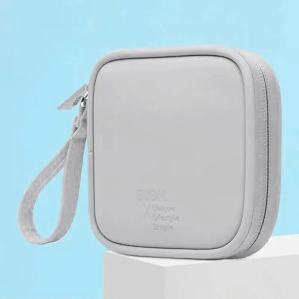 Estuche portátil multifuncional de auriculares gris claro con correa sobre una superficie blanca.