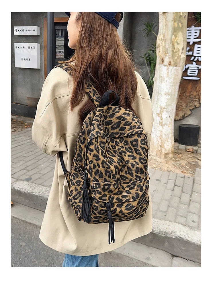 A woman wearing a beige shirt carries a leopard print canvas backpack outdoors.