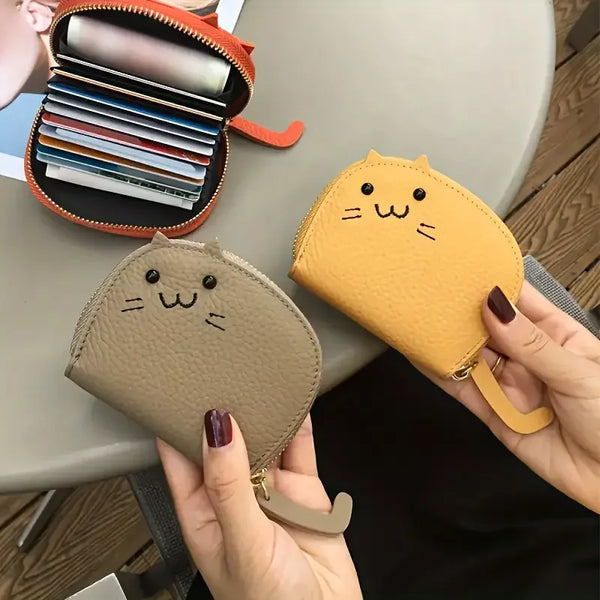 Una mano sostiene una cartera multi-tarjetas de gato de dibujos animados color canela junto a un portadaptadores naranja abie