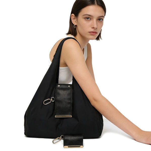 Une femme tient un sac de courses noir en nylon pliable avec des éléments métalliques dorés.