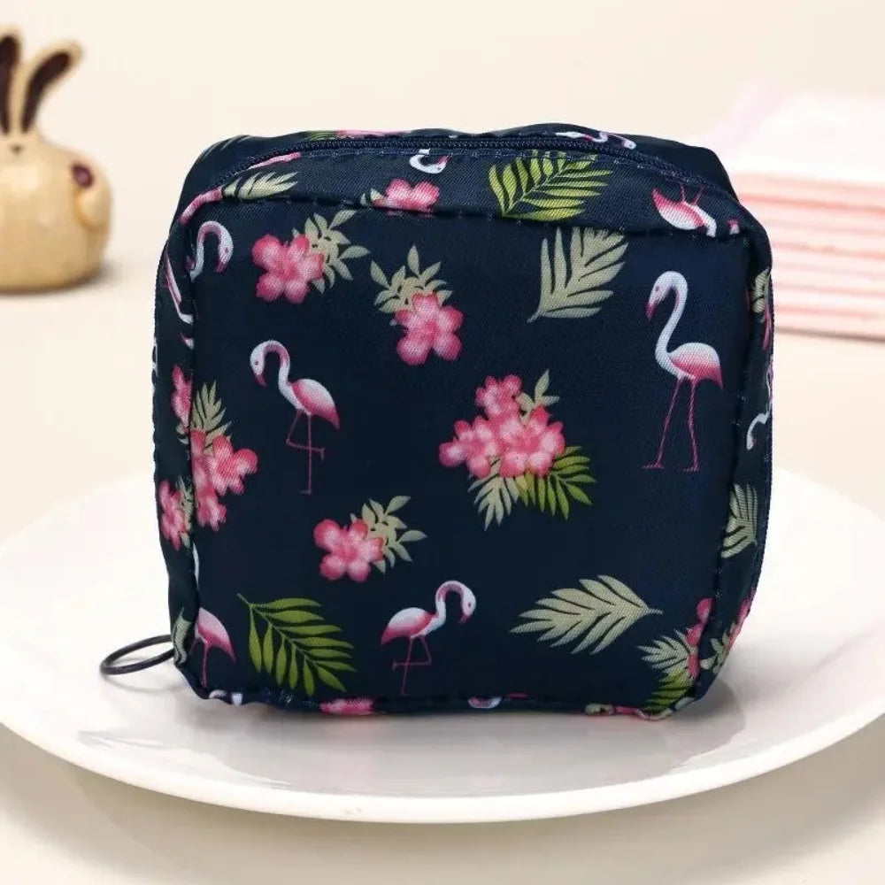 A dark blue pouch with a floral pattern featuring pink and green leaves, used for storing sanitary napkins.
