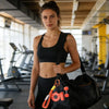 A woman in athletic wear holds a black gym bag with an orange dumbbell keychain charm.