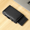 Black slim RFID-blocking carbon fiber card holder lying on a light wooden surface.