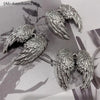 Silver metal angel wing keychain charms resting on a dark background with foliage.