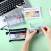 A hand is opening a clear zippered pouch containing various cards and coins, next to other similar pouches.