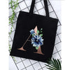 Black canvas tote bag featuring a floral print design with blue and green leaves.