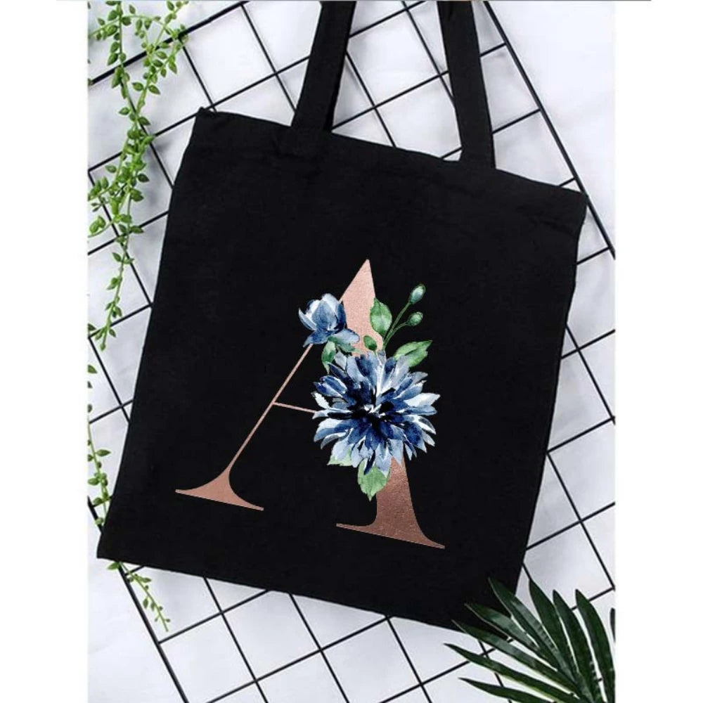 Black canvas tote bag featuring a floral print design with blue and green leaves.