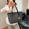 A woman holds a black faux leather tote bag with a monogram print against a light background.