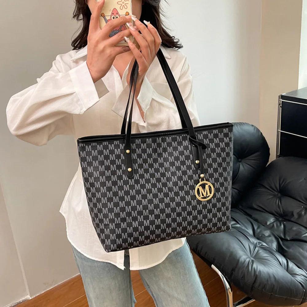 A woman holds a black faux leather tote bag with a monogram print against a light background.