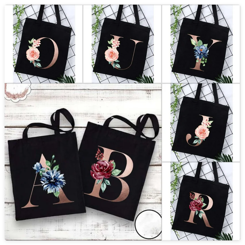A set of black canvas tote bags featuring an alphabet initial and floral design in rose and blue tones.