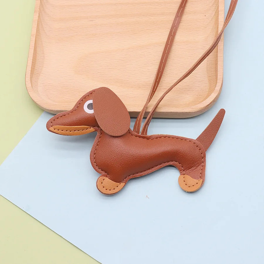 A brown leather dachshund dog charm keychain resting on a light wooden tray and blue paper.