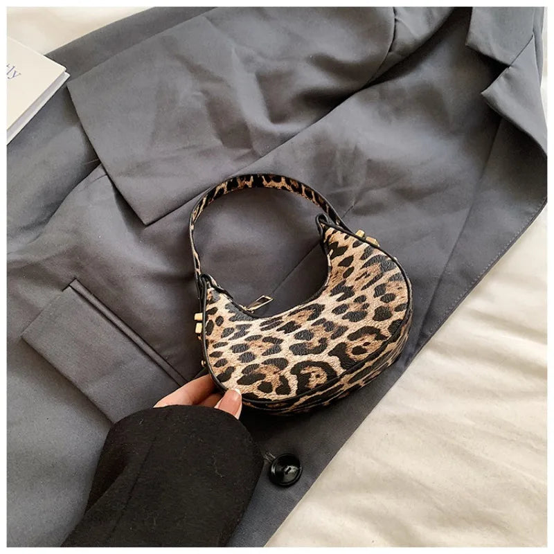 A hand holds a leopard print PU leather mini tote handbag against a gray blazer.