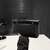Una mano sostiene un elegante bolso de mano tejido negro contra un fondo oscuro texturizado.