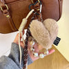 A brown leather heart pendant keychain featuring a fluffy suede charm and a long beige tassel, held by a hand.