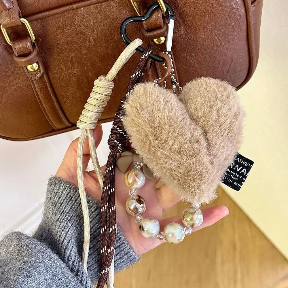 A brown leather heart pendant keychain featuring a fluffy suede charm and a long beige tassel, held by a hand.