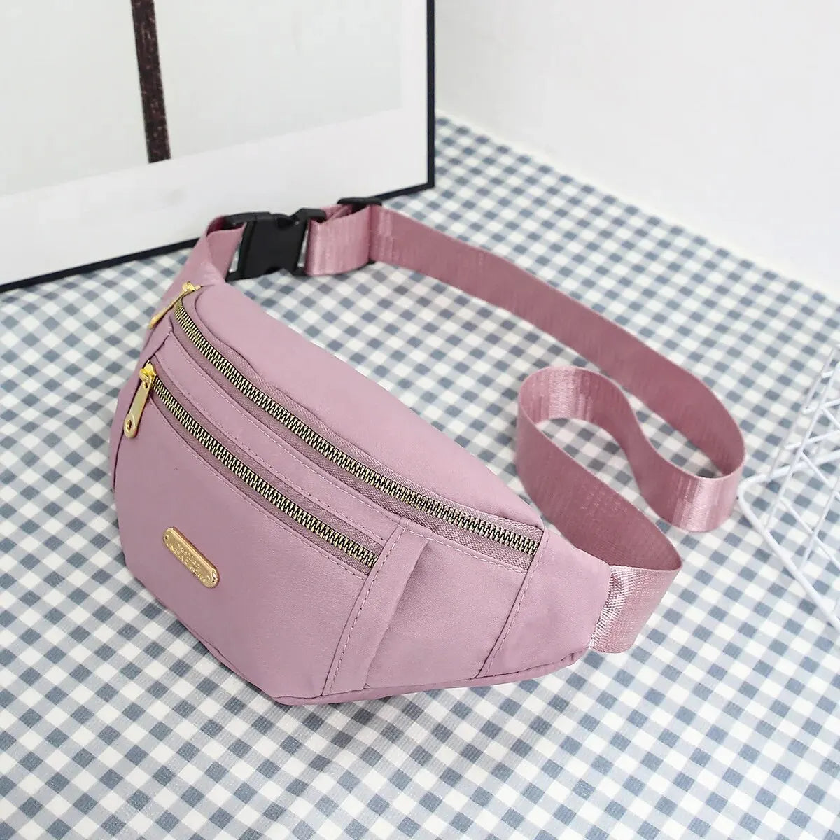 A pink multi-layer sports waist bag with a zipper and strap is displayed on a checkered surface.
