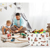 A man is sitting on the floor with a toddler playing with toys inside a white fabric storage basket.